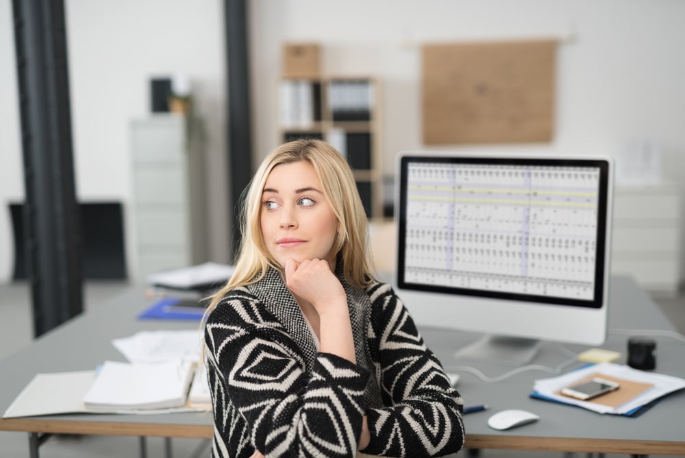 Young woman sitting in the office daydreaming turning in her chair to stare pensively off to the side with a serious expression and her chin resting on her hand